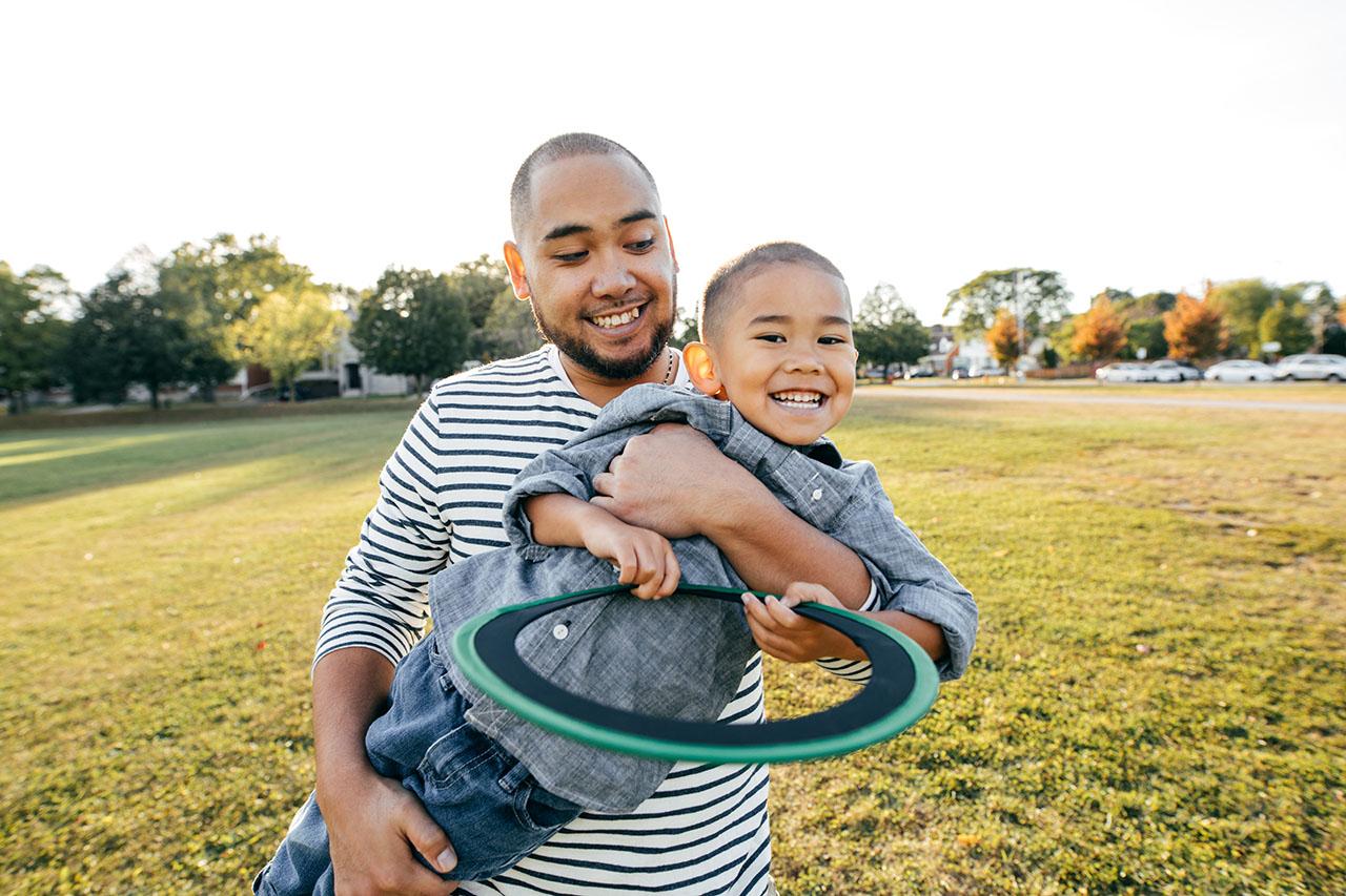 Father holding child in a field playing frisbee.